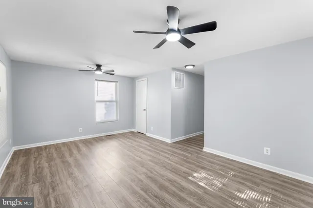 an empty room with wooden floor ceiling fan and windows