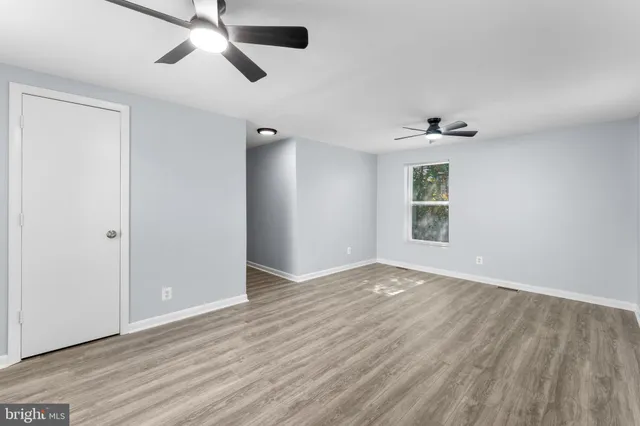 an empty room with wooden floor chandelier fan and windows
