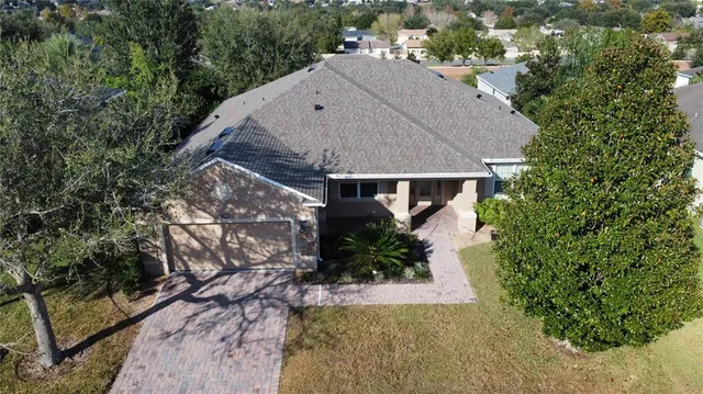an aerial view of a house with yard and trees in the background