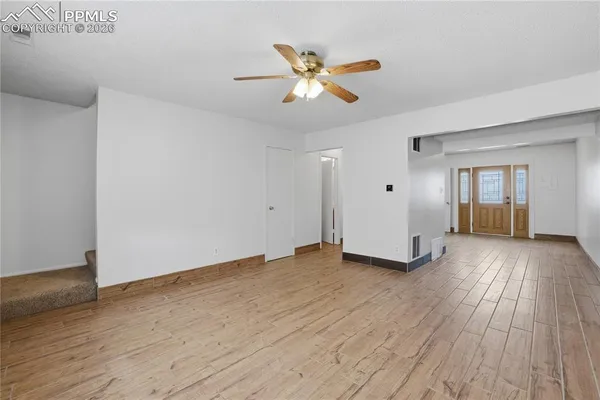 a view of an empty room with wooden floor and a ceiling fan