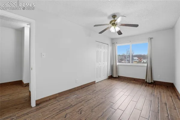 a view of an empty room with wooden floor and a ceiling fan