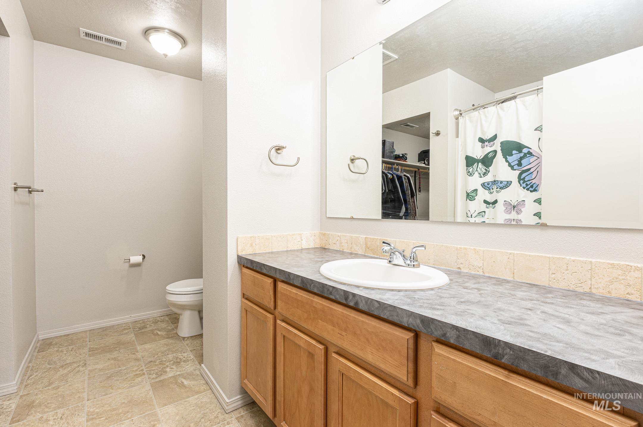 643 North Manship Avenue Meridian, ID 83642 - Photo 16 of 32 Bathroom with vanity, a shower with shower curtain, a walk in closet, stone finish floors, and a textured ceiling