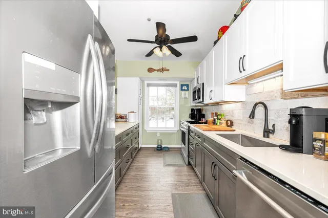 a kitchen with stainless steel appliances a sink dishwasher a refrigerator and white cabinets with wooden floor
