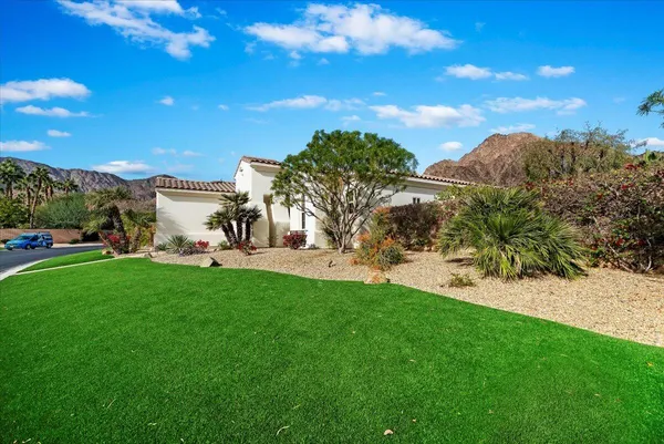 a view of a white house with a big yard plants and palm trees