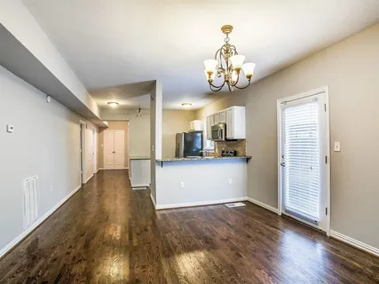 a view of an empty room and kitchen with wooden floor