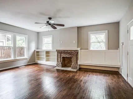 an empty room with wooden floor fireplace and windows