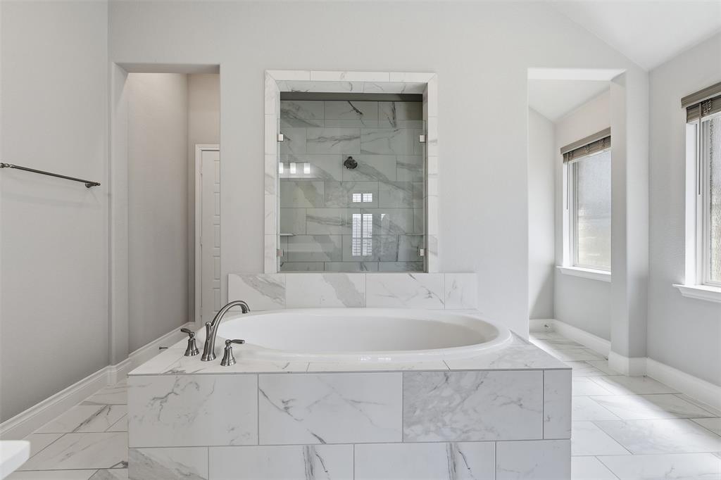 5640 Pradera Road Fort Worth, TX 76126 - Photo 18 of 35 Soaking tub with brushed nickel fixtures, glass-enclosed shower with tiled walls, and white tiled flooring