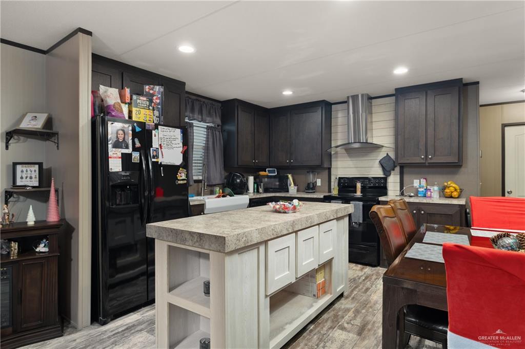 3118 Primrose Drive Weslaco, TX 78596 - Photo 4 of 12 Kitchen featuring wall chimney exhaust hood, black appliances, light countertops, light wood-type flooring, and a center island