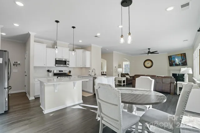 a kitchen with stainless steel appliances kitchen island granite countertop a dining table chairs and a refrigerator