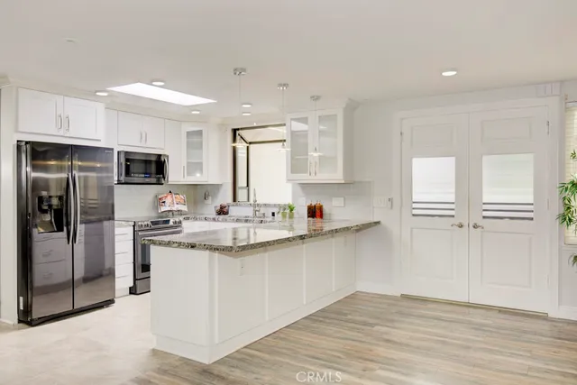 a kitchen with stainless steel appliances granite countertop a stove top oven a refrigerator and white cabinets with wooden floor