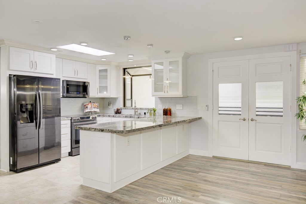 a kitchen with stainless steel appliances granite countertop a stove top oven a refrigerator and white cabinets with wooden floor