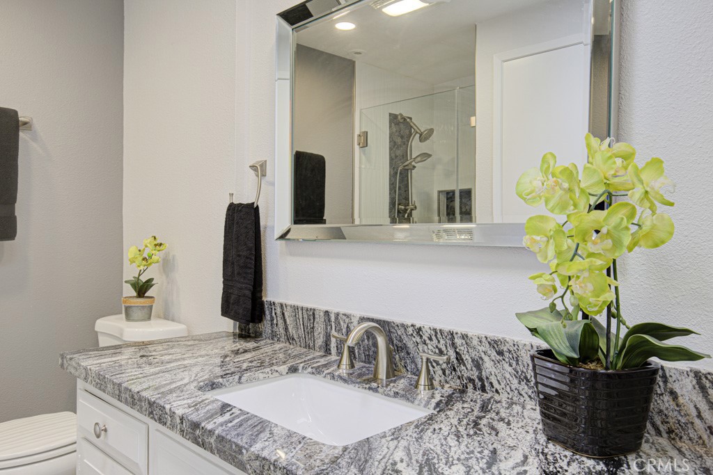 245 Calle Aragon, Unit C Laguna Woods, CA 92637 - Photo 15 of 32 a bathroom with a granite countertop sink a toilet and mirror