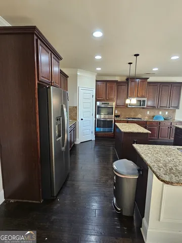 a kitchen with stainless steel appliances granite countertop a refrigerator a sink a stove and a wooden cabinets