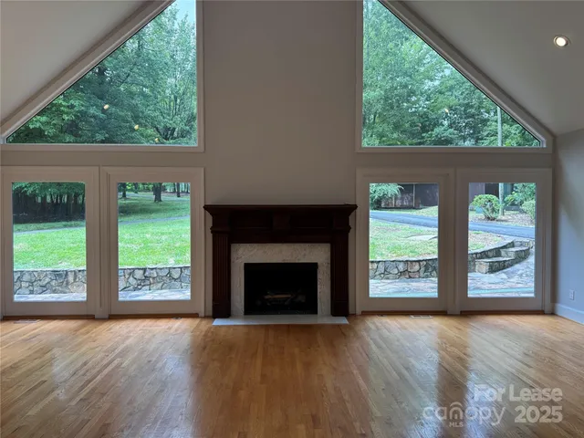 an empty room with wooden floor fireplace windows and outdoor view