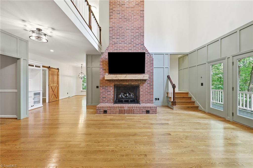 8861 Boylston Road Colfax, NC 27235 - Photo 10 of 50 A soaring vaulted great room showcases a striking floor-to-ceiling brick fireplace, extensive custom millwork, hardwood floors, and seamless connections to the surrounding living spaces. (Rear porch entrance on right side)