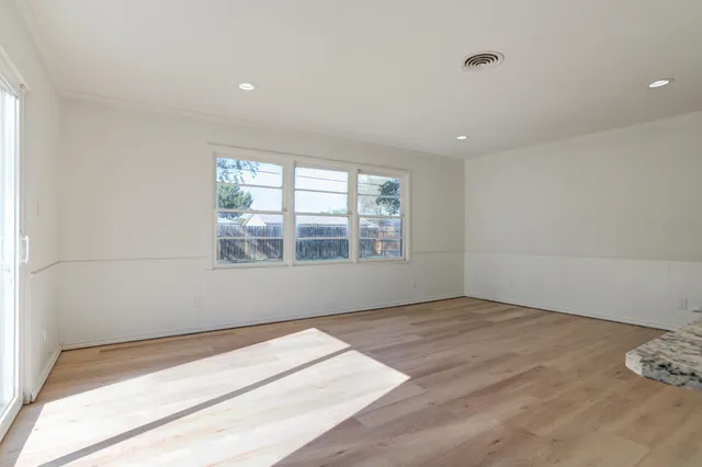 an empty room with wooden floor and kitchen view