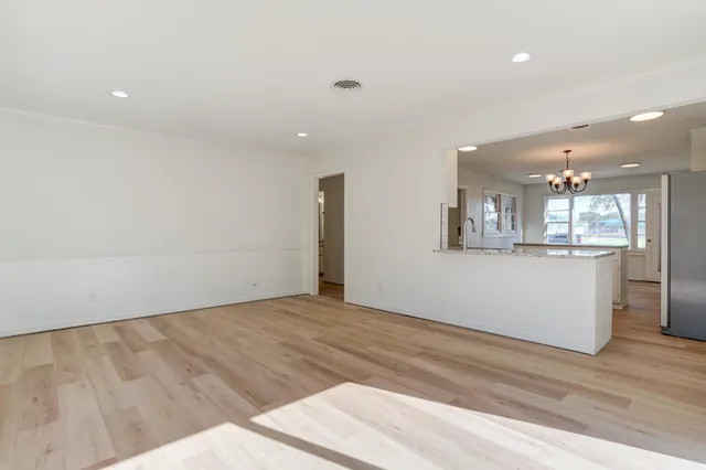 an empty room with wooden floor and kitchen view