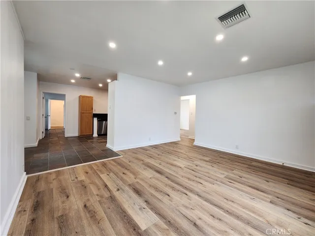 a view of an empty room with wooden floor and a kitchen