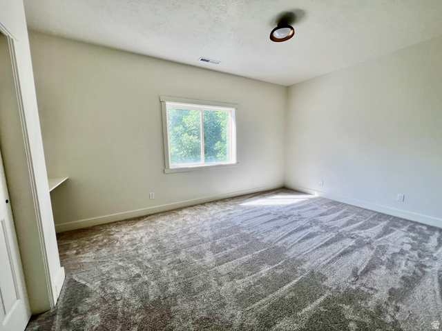 812 East Bates Cyn Road Tooele, UT 84074 - Photo 64 of 144 Spacious room featuring neutral-toned walls, textured gray carpeting, a large window, a built-in desk, and a ceiling-mounted light fixture