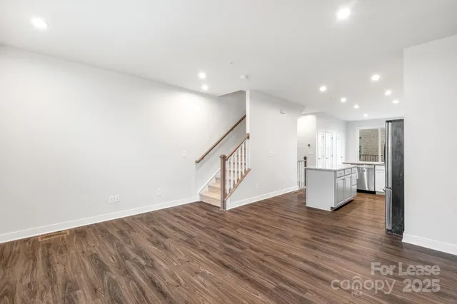 a view of an empty room with wooden floor and a kitchen