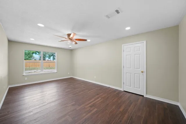 an empty room with wooden floor a ceiling fan and windows