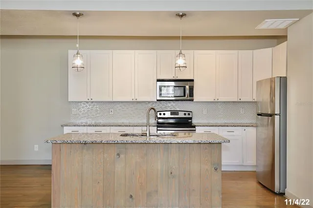 a kitchen with stainless steel appliances granite countertop a refrigerator a stove and white cabinets with wooden floor