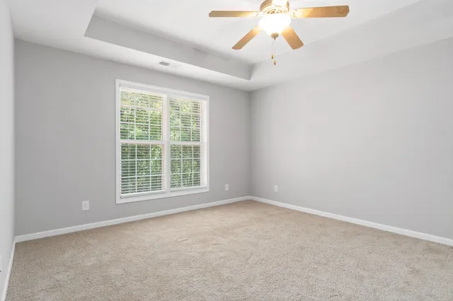 an empty room with chandelier fan and windows