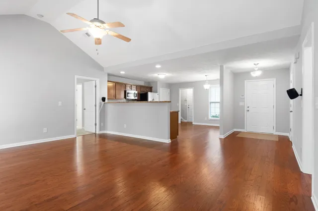 a view of an empty room with wooden floor and a kitchen