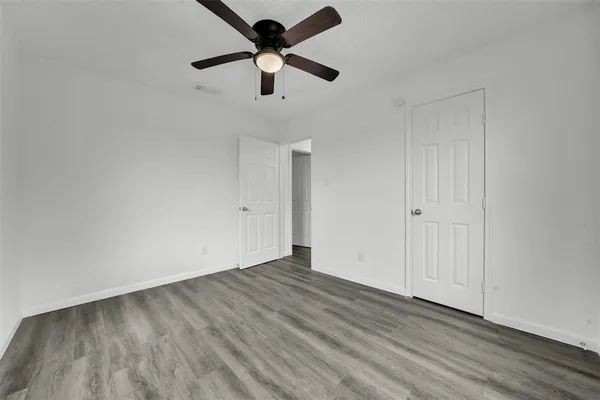an empty room with wooden floor ceiling fan and windows