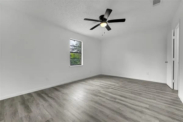 an empty room with wooden floor fan and windows