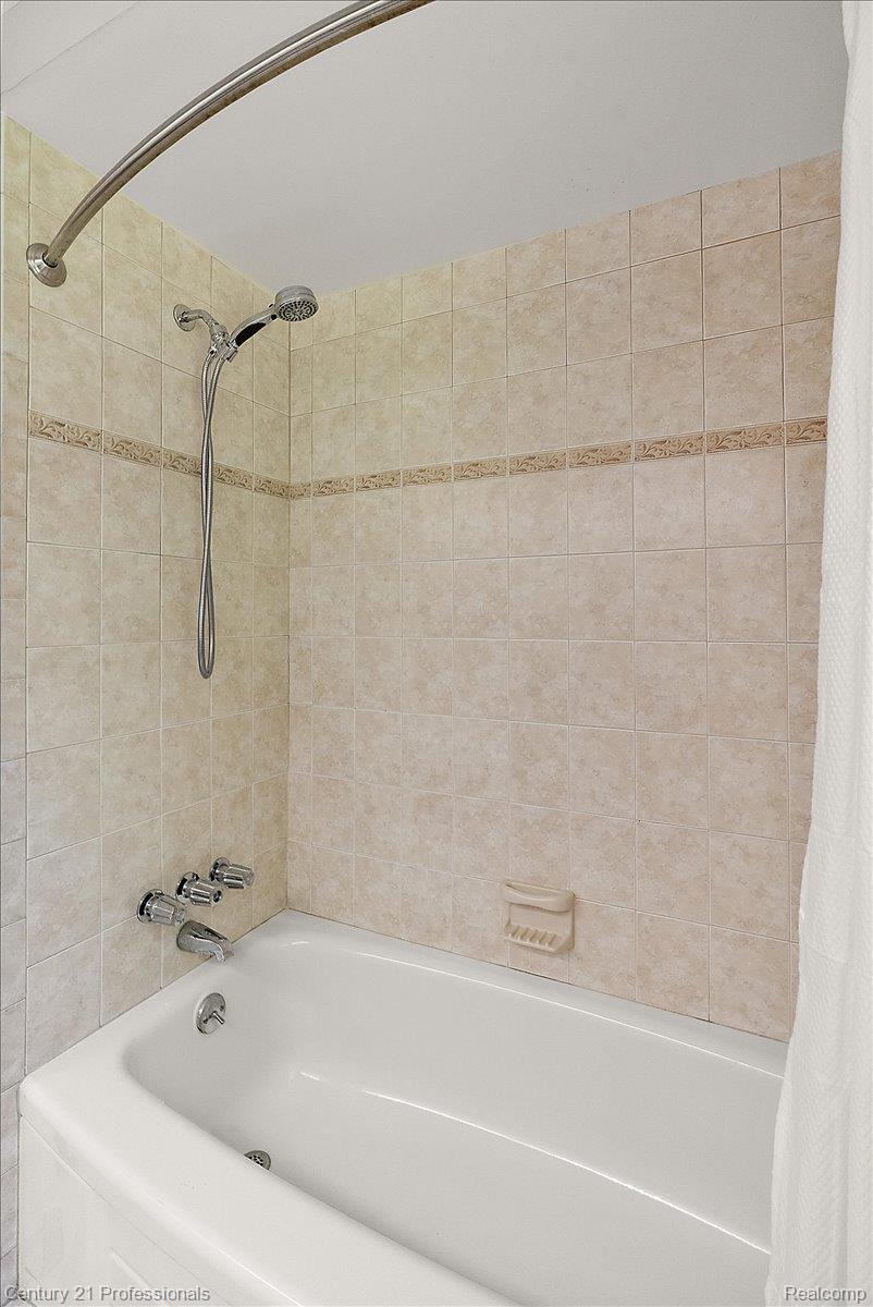633 Foxhall Road Bloomfield Hills, MI 48304 - Photo 55 of 61 White alcove bathtub featuring a chrome showerhead with a handheld sprayer, chrome faucet, and tiled surround with a decorative accent band