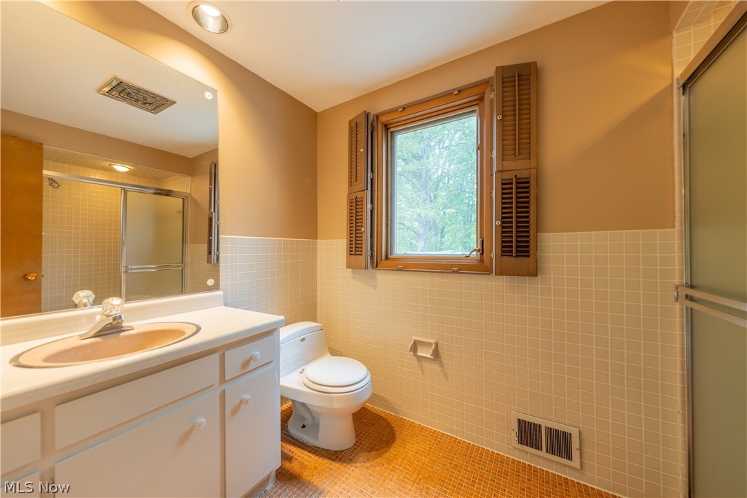 25001 Letchworth Road Beachwood, OH 44122 - Photo 37 of 50 Bathroom featuring a white vanity with a built-in sink, a wall-mounted mirror, a toilet, a window with wooden shutters, and a shower with a sliding glass door