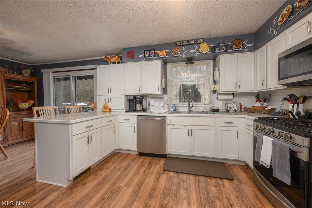390 Ross Road Waynesburg, OH 44688 - Photo 5 of 30 Kitchen with a peninsula, stainless steel appliances, white cabinets, a textured ceiling, and light countertops