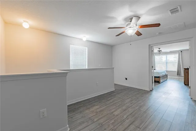 an empty room with wooden floor fan and windows