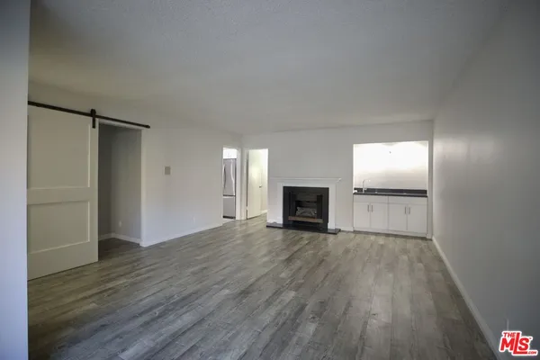 a view of an empty room with wooden floor fireplace and a window