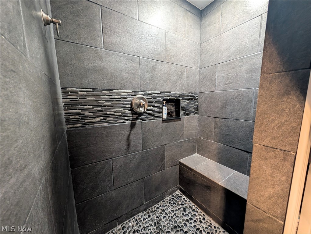 6700 McCaslin Road Nashport, OH 43830 - Photo 23 of 30 Shower featuring large format dark grey tile, a mosaic tile accent band, a built-in shower bench, a recessed niche, and a pebble tile floor