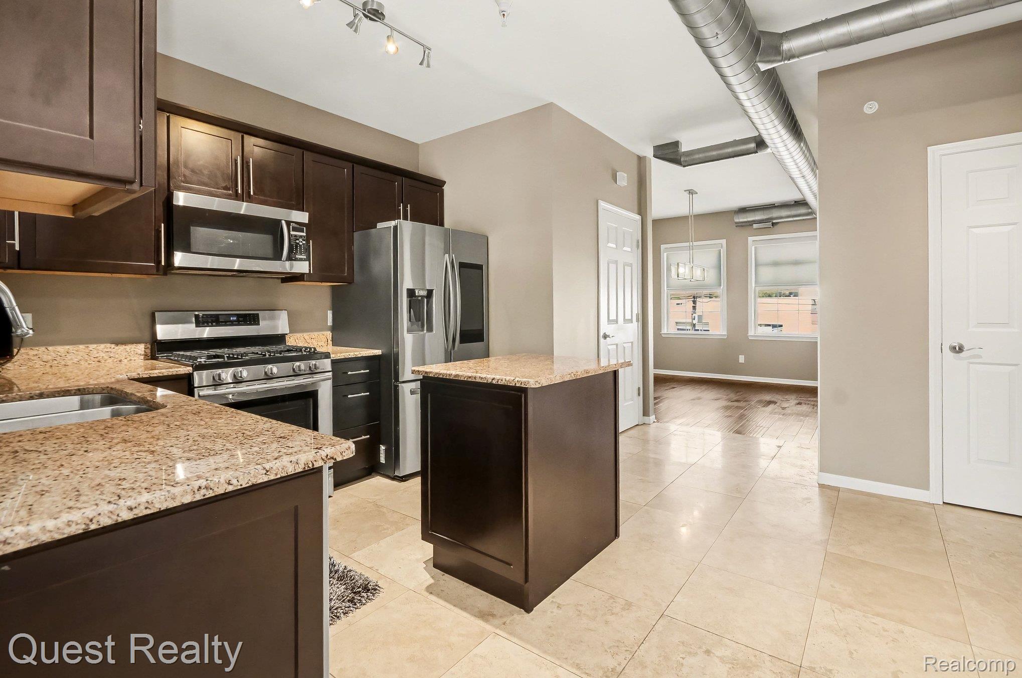218 Mill Street Rochester, MI 48307 - Photo 11 of 34 Kitchen with dark wood finish cabinetry, a center island, stainless steel appliances, light stone countertops, and hanging light fixtures