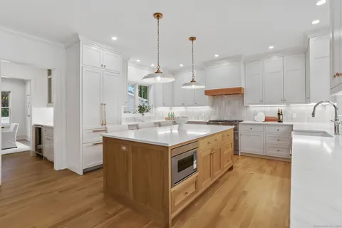 a kitchen with kitchen island a sink stove a refrigerator and white cabinets with wooden floor