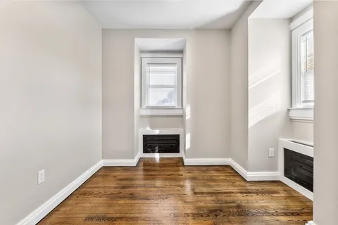 a view of an empty room with wooden floor fireplace and a window