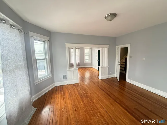 a view of an empty room with wooden floor and a window