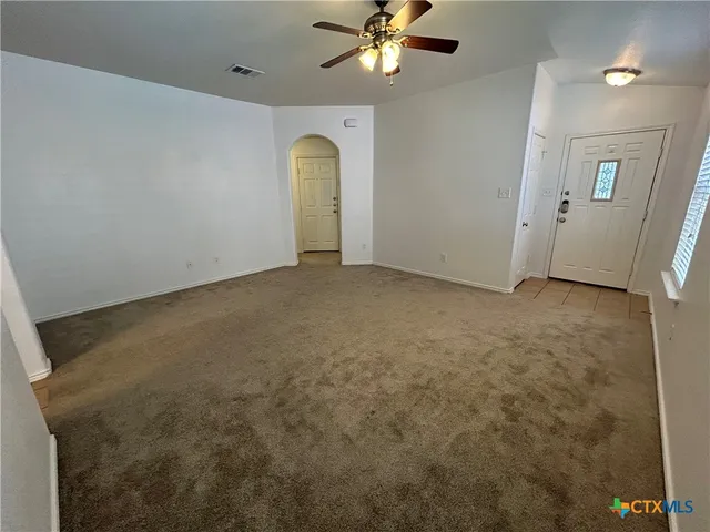 an empty room with a chandelier fan and windows