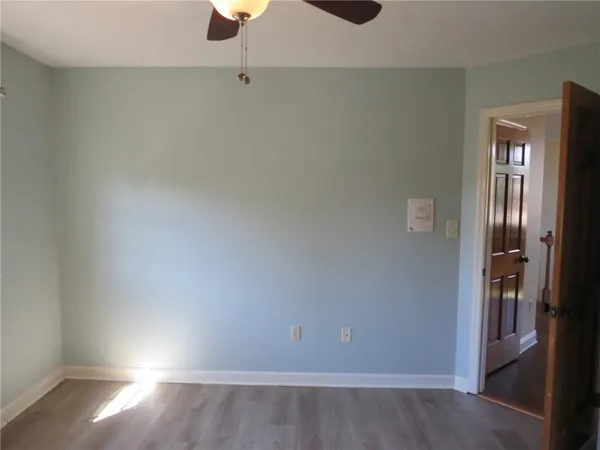 an empty room with a chandelier fan and wooden floor