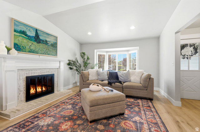 1405 Vintry Lane Murray, UT 84121 - Photo 7 of 44 Living area featuring a fireplace with a white mantel and light brick surround, wood-finish flooring, a vaulted ceiling, recessed lighting, and a bay window with plantation shutters
