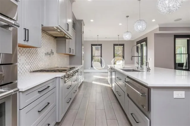 a large kitchen with stainless steel appliances kitchen island granite countertop a stove a sink a refrigerator and white cabinets with wooden floor