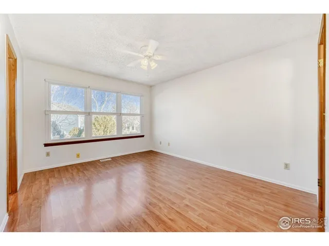 an empty room with wooden floor chandelier fan and windows
