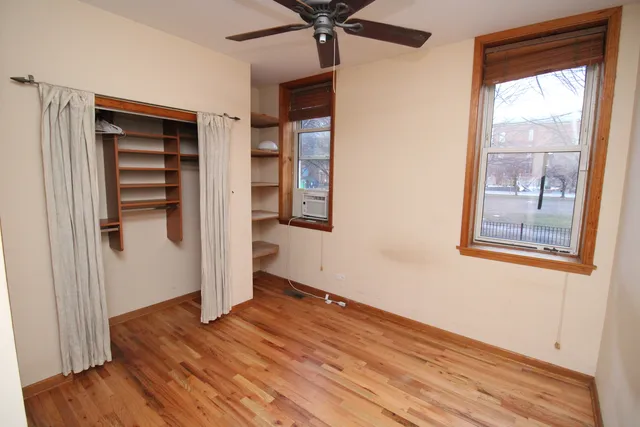 a view of an empty room with wooden floor and a ceiling fan