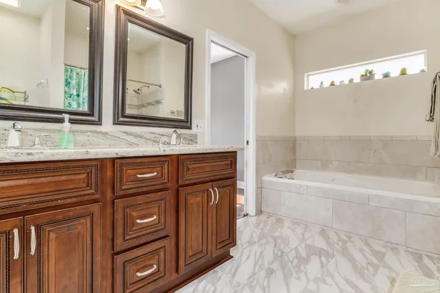 a bathroom with a granite countertop sink a mirror a bathtub and next to a window