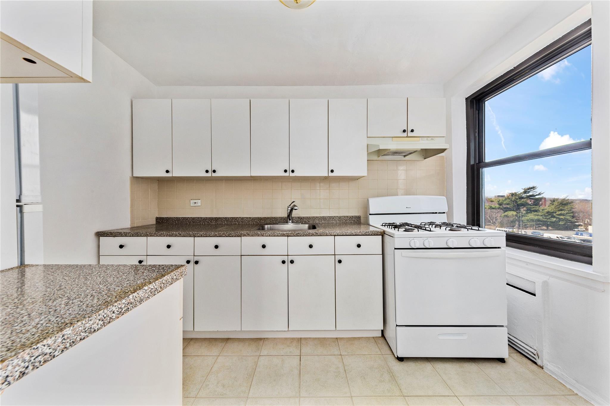 73-62 Bell Boulevard, Unit 4K Queens, NY 11364 - Photo 11 of 16 Kitchen with under cabinet range hood, white cabinetry, gas range gas stove, and a sink