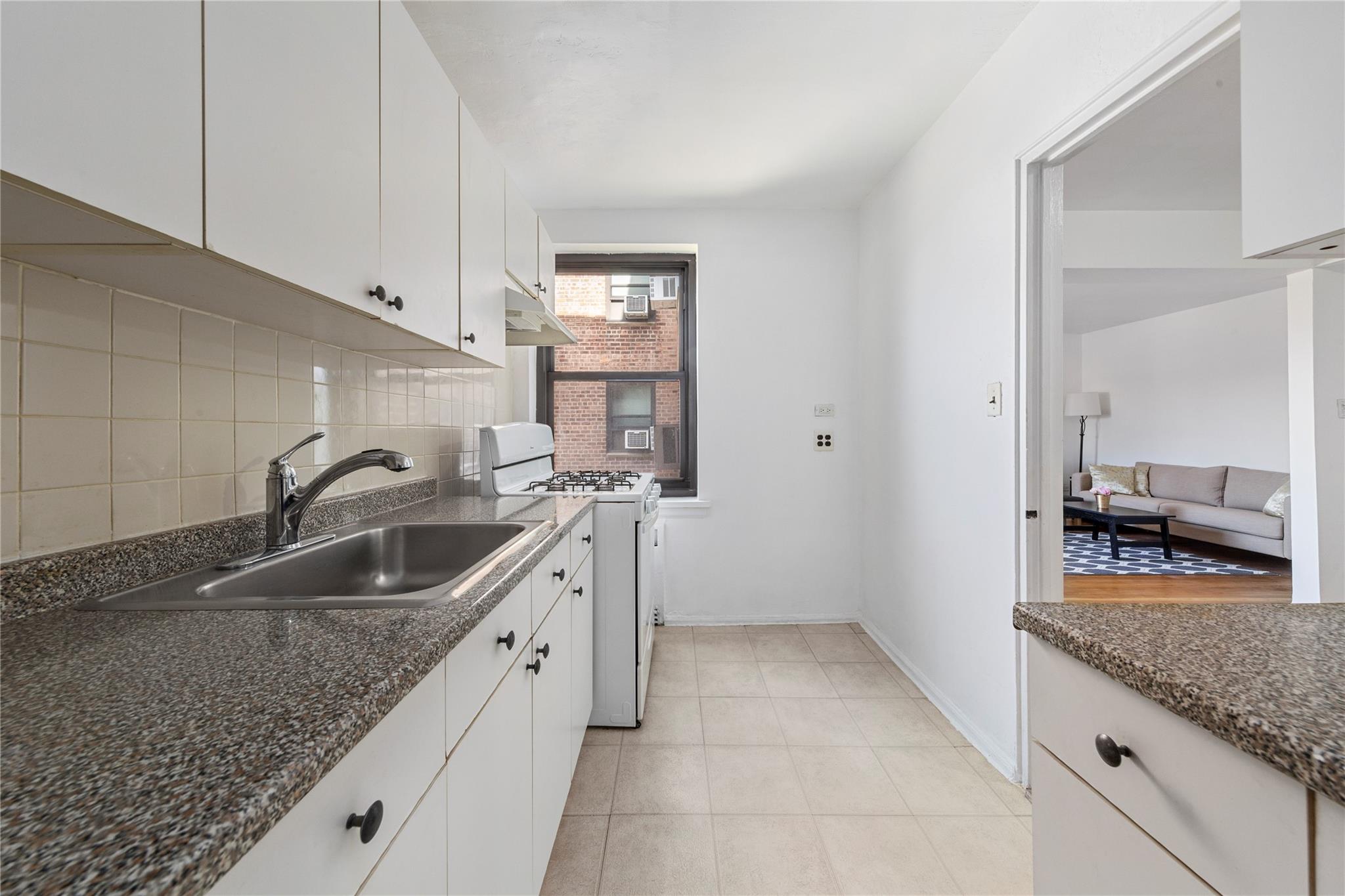 73-62 Bell Boulevard, Unit 4K Queens, NY 11364 - Photo 12 of 16 Kitchen featuring a sink, under cabinet range hood, backsplash, white cabinetry, and white gas range