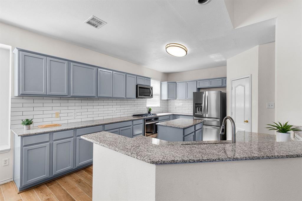 2700 Hereford Road Denton, TX 76210 - Photo 4 of 36 Kitchen featuring gray shaker-style cabinetry, granite countertops, white subway tile backsplash, stainless steel appliances, and wood-finish flooring